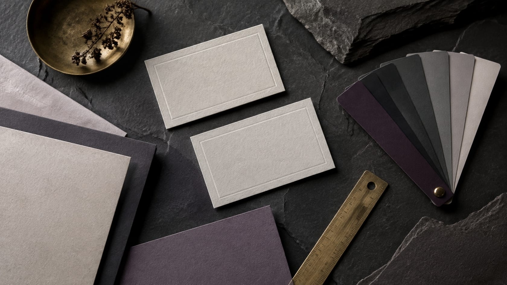Blank business cards, paper stock and colour swatches laid out on dark slate